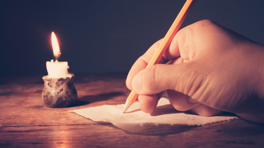 person's hand writing a letter candle in background